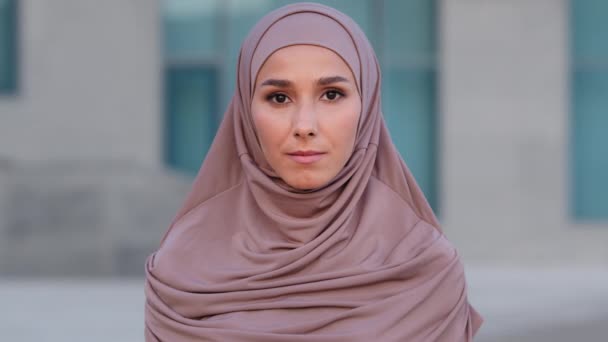 Ritratto femminile all'aperto vicino ragazza islamica musulmana giovane donna adulta donna etnica indossa hijab beige vestiti tradizionali guardando la fotocamera in piedi sulla strada città calma espressione facciale - Filmati, video