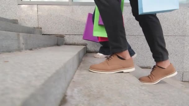 Deux paires de pieds jambes masculines et féminines dans des chaussures à la mode marchent pas en ville dans le centre commercial magasin portent des sacs d'achats lumineux, acheteurs méconnaissables clients marchant pas à pas, rabais de vente - Séquence, vidéo