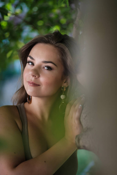 Headshot of young woman between trees. The trees are out of focus. - Photo, Image