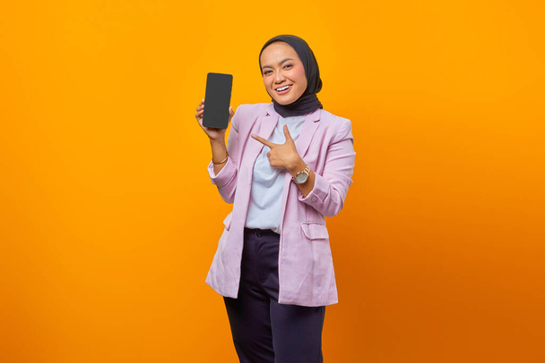 Retrato de una mujer asiática bastante joven apuntando alegremente en el teléfono inteligente con su dedo - Foto, imagen