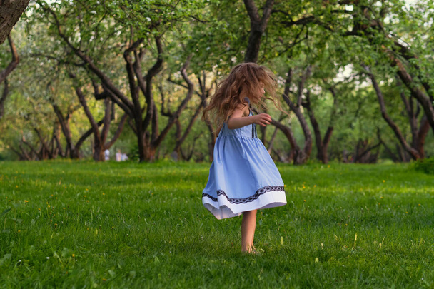 Το κοριτσάκι τρέχει ξυπόλητο στο γρασίδι. χαρούμενο παιδί σε μια ζεστή καλοκαιρινή μέρα. - Φωτογραφία, εικόνα