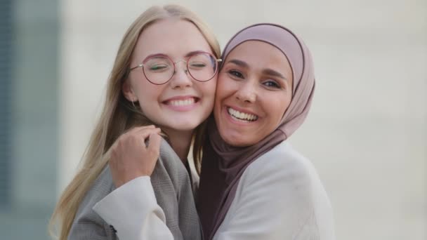 Zwei glücklich lächelnde verschiedene junge Freundinnen oder Kolleginnen, die sich umarmen, glücklich, einander zu treffen. Millennial indisches Mädchen im Hijab und junge blonde Europäerin zusammen. Feminismus, Konzept für internationale Beziehungen - Filmmaterial, Video