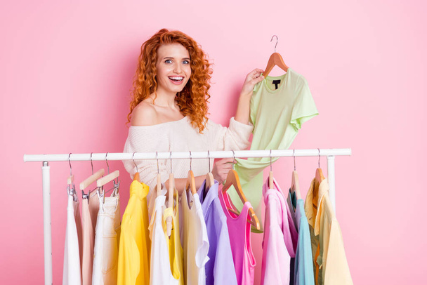 Retrato fotográfico de chica pelirroja asombrada alegre haciendo compras en boutique seleccionando ropa aislada de color rosa pastel fondo - Foto, imagen