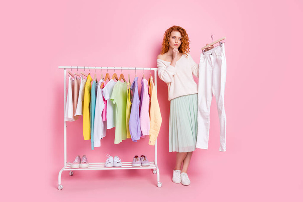 Full length photo of young girl think choice look trousers clothes shopping isolated over pink color background - 写真・画像