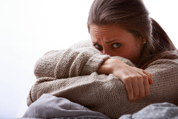 Troubled or sick young woman hiding her face in her arm looking at the camera with wide eyes and an anxious frown in a cropped closeup portrait - Foto, imagen