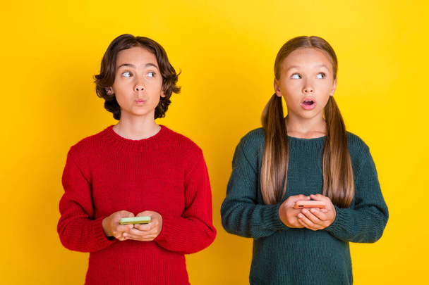 Photo portrait two children amazed using cellphones looking blank space isolated vivid yellow color background - Valokuva, kuva
