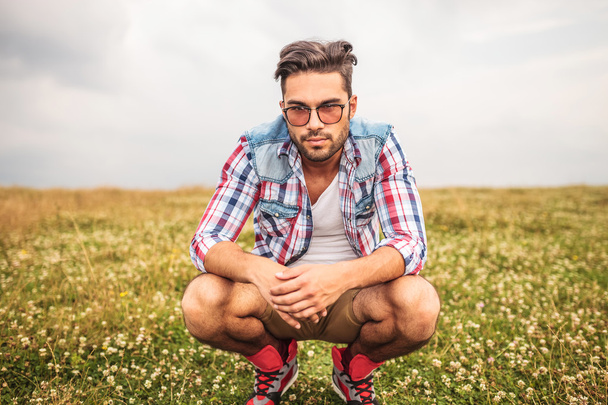 serio uomo casuale accovacciato in un campo d'erba
 - Foto, immagini