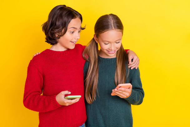 Portret van twee mooie knappe vrolijke vrienden knuffelen met behulp van apparaat chatten geïsoleerd over helder gele kleur achtergrond - Foto, afbeelding
