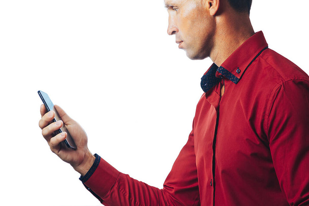A businessman in a red shirt with a mobile phone stands isolated on a white background - Foto, Imagen