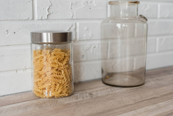 Wooden kitchen room. Macaroni in glass jars on shelf on kitchen wall. Cookware concept, kitchenware - Foto, afbeelding