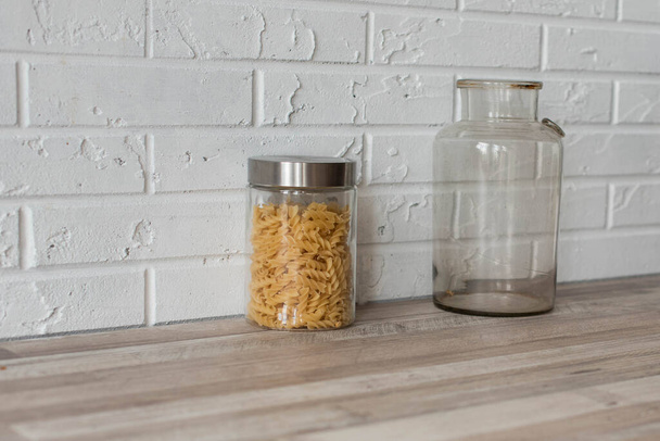 Wooden kitchen room. Macaroni in glass jars on shelf on kitchen wall. Cookware concept, kitchenware - Photo, Image