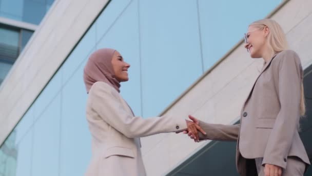 Glückliche muslimische Geschäftsfrau Verkäuferin im Hijab schüttelt der tausendjährigen kaukasischen Kundin die Hand und schließt beim Treffen mit verschiedenen Frauen Partnerschafts-, Respekt- und Kooperationskonzept mit einer Kundin ab - Filmmaterial, Video