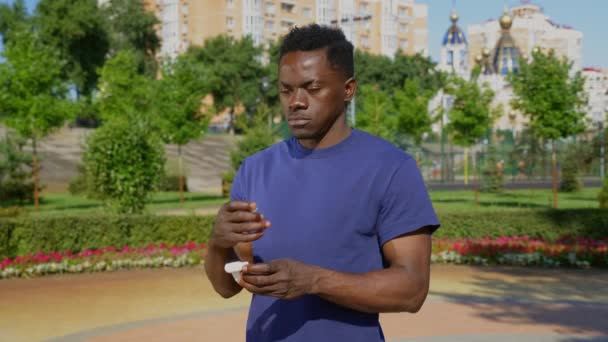Portré Afro-amerikai felnőtt férfi áll a parkban visel vezeték nélküli fülhallgató - Felvétel, videó