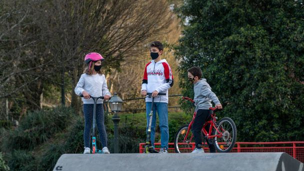 VIGO, SPAIN - Mar 07, 2021: A girl and two boys in a mask with skates and bicycles in a park in Vigo, Spain - Foto, imagen
