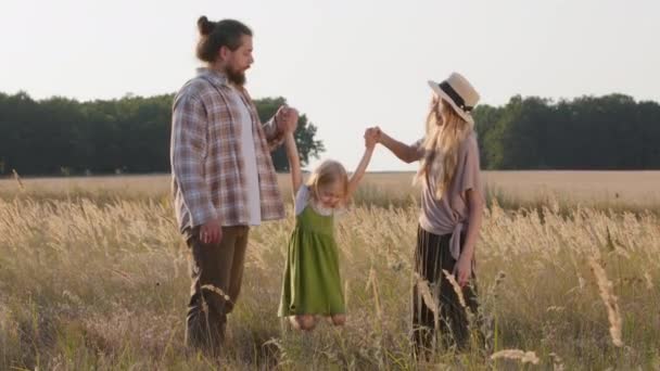 Mutlu Kafkas ailesi üç çocuklu aile doğada buğday tarlasında duruyor erkek ve kız çocuk dışarıda oynuyorlar kız ve erkek el ele tutuşuyorlar bebek kızlarını hava salıncaklı uçuş oyununa sokuyorlar - Video, Çekim