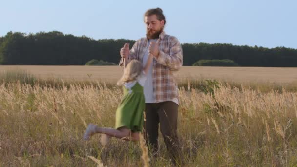 Mladý táta běloch muž otec táta drží dítě dcera holčička podle ramen rotuje vířící dítě dítě ve vzduchu hraje hru v pšeničném poli s dětmi venku, rodina pojetí sblížení - Záběry, video