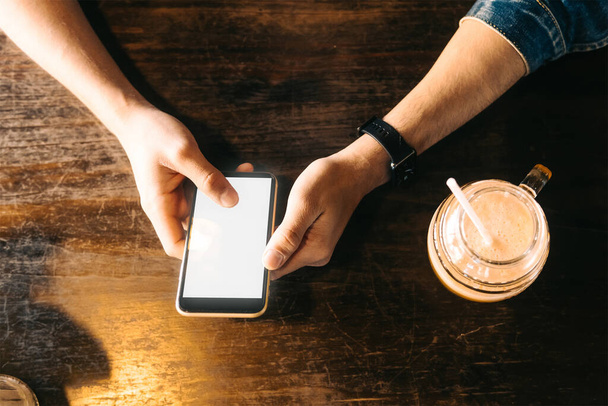 A top view of male hands holding a smartphone and a drink on a wooden table - Foto, Bild