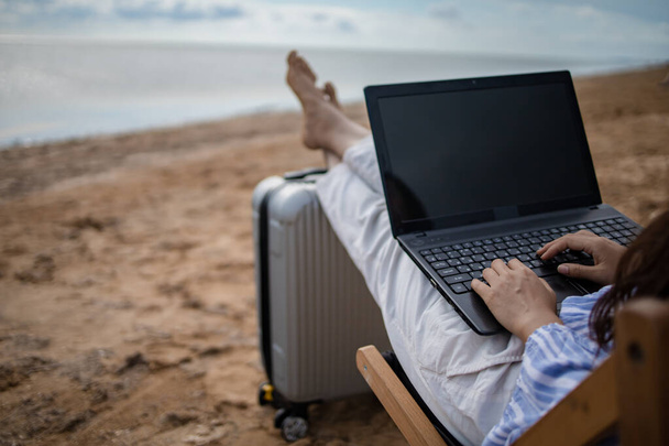 Молодая азиатка с планшетным компьютером во время тропического отдыха на пляже. Фрилансер работает на ноутбуке, лежа на солнцепеке. - Фото, изображение