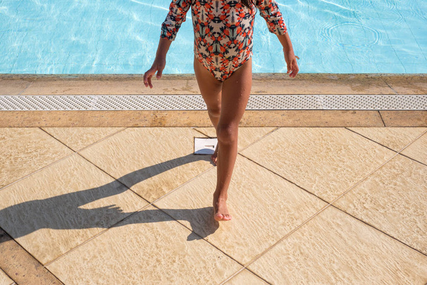 A closeup shot of a little girl in a swimsuit walking on a platform near the pool - Photo, image