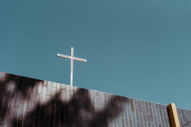 a low angle shot of a metallic cross on a structure under blue sky - Photo, image