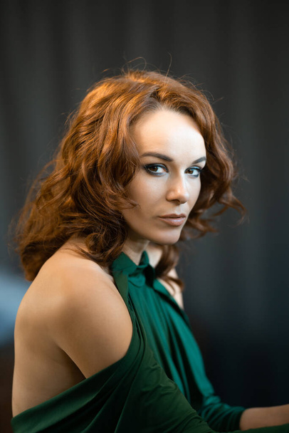A portrait of a pretty brunette female in green drees staring at the camera on the gray background - Фото, зображення