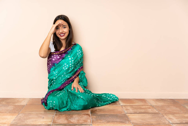 Young Indian woman sitting on the floor saluting with hand with happy expression - Foto, afbeelding