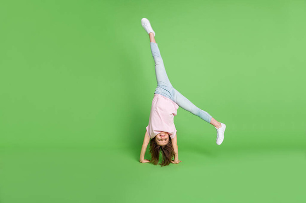 Full body photo of young little girl stand on hand acrobat sporty training isolated over green color background - Foto, afbeelding