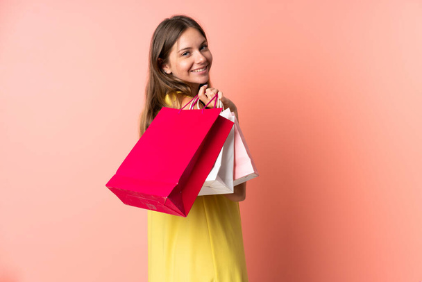 Young Lithuanian woman isolated on pink background holding shopping bags and smiling - Photo, Image