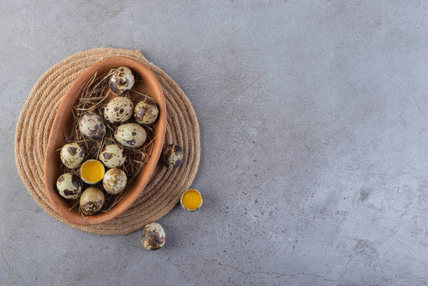 Ένα καφέ πιάτο γεμάτο ωμά αυγά ορτυκιού πάνω σε πέτρινο τραπέζι. Υψηλής ποιότητας φωτογραφία - Φωτογραφία, εικόνα