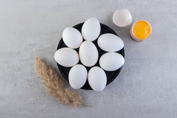 Raw white chicken eggs with yolk and wheat ears placed on stone table. High quality photo - Foto, Imagem