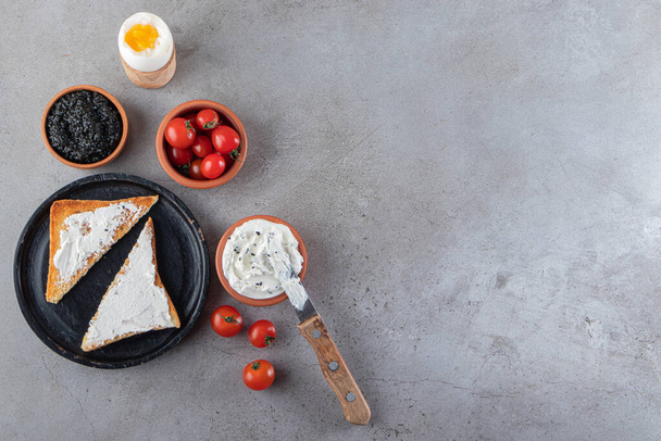 Toast con burro e pomodorini rossi posti su fondo marmoreo  - Foto, immagini