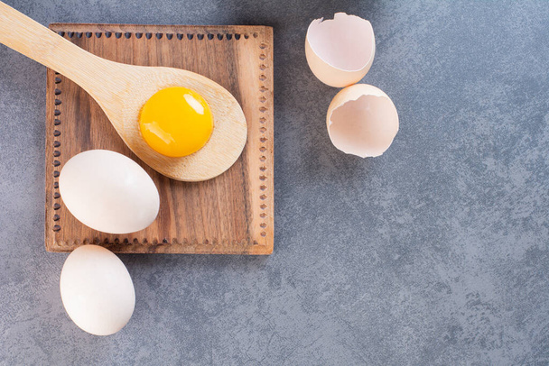 Wooden spoon with yolk and chicken eggs on stone background. High quality photo - Zdjęcie, obraz