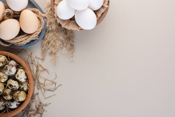 Schalen mit rohen Hühner- und Wachteleiern mit Mehl auf beigem Hintergrund. Hochwertiges Foto - Foto, Bild