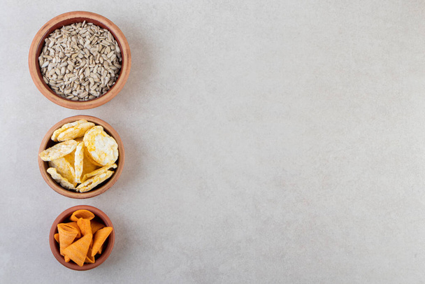 Bowls of chips, crackers and sunflower seeds on stone surface. High quality photo - Photo, Image