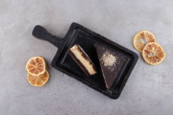 Pieces of chocolate cake with dried slices of lemon placed on stone table. High quality photo - Photo, Image