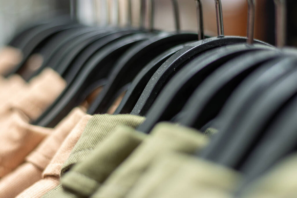 Kleiderbügel in einer Reihe und Bekleidung. Einzelhandelskonzept, Kleiderbügel in sehr weichem und selektivem Fokus. Schwarze Kleiderbügel und Kleidungsteile hintereinander. - Foto, Bild