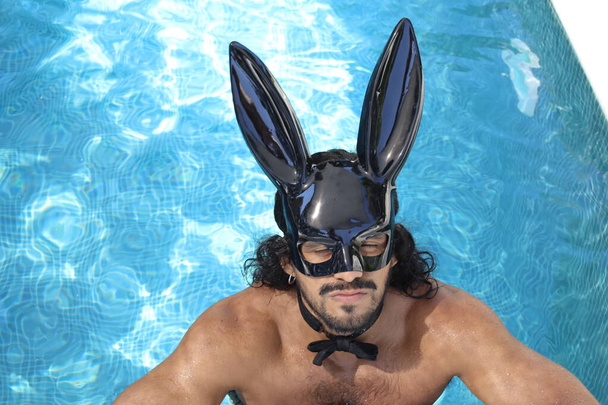 primer plano retrato de guapo joven mestizo sin camisa hombre con máscara de conejo en la piscina - Foto, Imagen