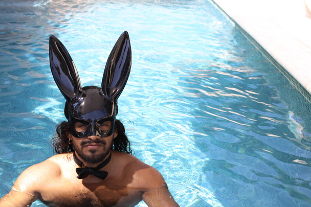 közeli kép jóképű fiatal vegyes fajú félmeztelen férfi nyuszi maszk medencében - Fotó, kép