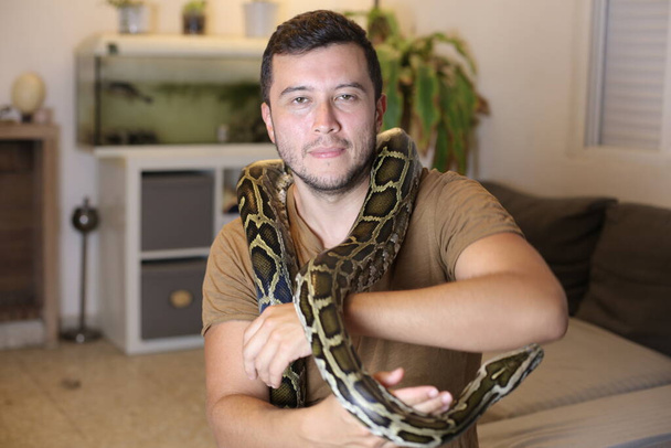 retrato de cerca del joven guapo con su serpiente mascota en casa - Foto, Imagen