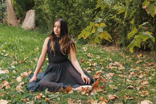 Esmer Latin bir kızın portresi. Gözleri kapalı parktaki kuru akçaağaç yaprakları üzerinde oturuyor. - Fotoğraf, Görsel