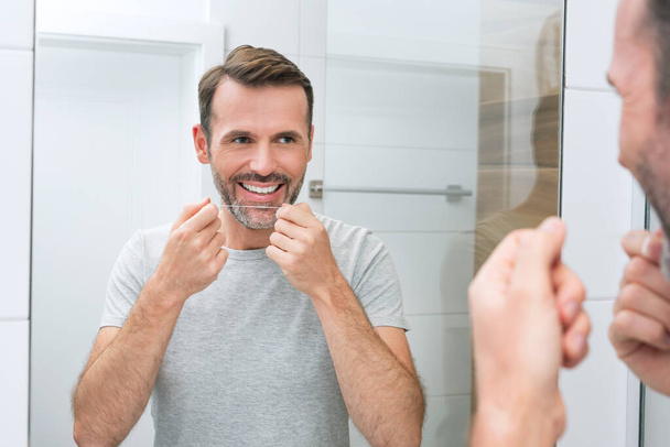 Man using dental floss in the bathroom. White teeth and a beautiful smile, morning hygiene concept - Foto, immagini
