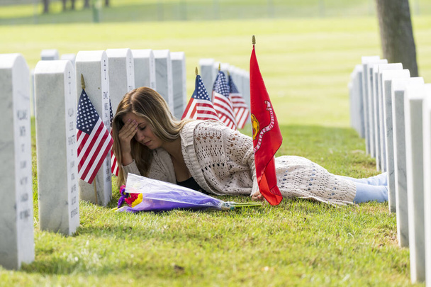 Молодая невеста показывает свое горе на месте захоронения члена семьи на военном кладбище - Фото, изображение