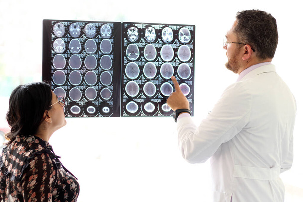 Lekarz medycyny specjalizujący się w neurologii wyjaśnia tomografię mózgu latynoskiej kobiecie w okularach w gabinecie. - Zdjęcie, obraz