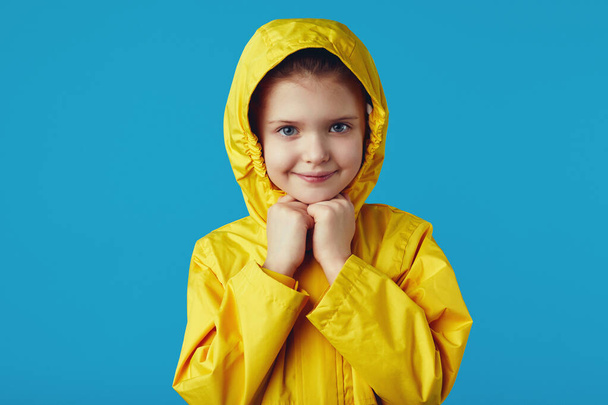 Enfant fille porte imperméable jaune imperméable, garde les mains ensemble sous le menton - Photo, image
