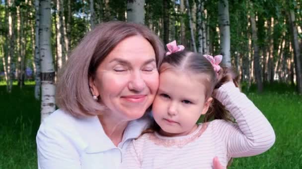 Porträt eines sich umarmenden Paares, Großmutter ihrer kleinen 3-jährigen Enkelin, lachend und einander sanft auf die Wangen drückend, gekleidet in hellweiß-rosa Kleidung. Das Konzept der Generationengerechtigkeit - Filmmaterial, Video