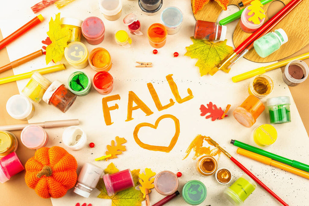 Creative autumn colors composition. Gouache, brushes, paper, traditional decor, and the word "fall". Art, good mood, hobby, or lifestyle. Light beige background, flat lay, top view - Foto, Imagem