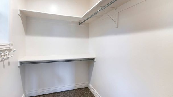 Pano Walk in closet with dark brown carpet flooring and wall mounted shelves and hooks - Photo, Image
