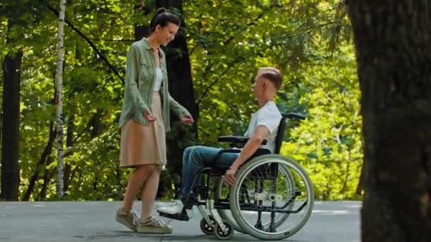 Homem deficiente em uma cadeira de rodas cavalga para sua amiga e abraçando-a - Filmagem, Vídeo