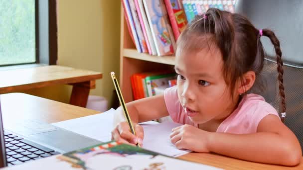 Nettes kleines Schulmädchen, das während ihres Online-Unterrichts zu Hause Hausaufgaben in Mathe lernt, soziale Distanzierung während des Coronavirus-Ausbruchs. Konzept der Online-Bildung oder der häuslichen Erziehung. - Filmmaterial, Video