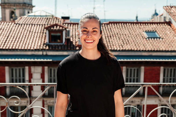 Young woman looking at camera with positive attitude on a rooftop in madrid with rooftops in the background. - Фото, изображение